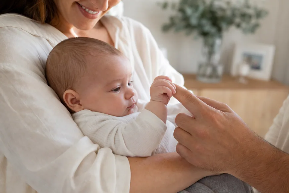 Baby gripping Dad's finger while safely cradled by Mum at home